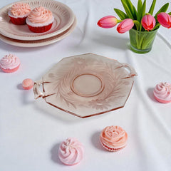 Vintage pink Depression glass serving dish with etched floral design and dual handles, styled on marble with soft lighting to highlight its shape, color, and collectible charm.