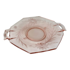 Vintage pink Depression glass serving dish with etched floral design and dual handles, styled on marble with soft lighting to highlight its shape, color, and collectible charm.