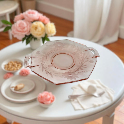 Vintage pink Depression glass serving dish with etched floral design and dual handles, styled on marble with soft lighting to highlight its shape, color, and collectible charm.