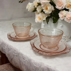 Vintage pink depression glass set featuring 2 delicate cups from the American Sweetheart collection and 2 square saucers from the Madrid collection, both adorned with intricate floral and geometric etched patterns. A timeless and sustainable addition to any table or décor.