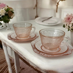 Vintage pink depression glass set featuring 2 delicate cups from the American Sweetheart collection and 2 square saucers from the Madrid collection, both adorned with intricate floral and geometric etched patterns. A timeless and sustainable addition to any table or décor.