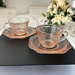 Vintage pink depression glass set featuring 2 delicate cups from the American Sweetheart collection and 2 square saucers from the Madrid collection, both adorned with intricate floral and geometric etched patterns. A timeless and sustainable addition to any table or décor.