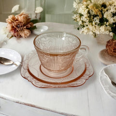 Vintage pink depression glass set featuring 2 delicate cups from the American Sweetheart collection and 2 square saucers from the Madrid collection, both adorned with intricate floral and geometric etched patterns. A timeless and sustainable addition to any table or décor.