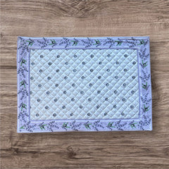 Reversible quilted cotton placemat in Lauris Light Yellow by Marat d’Avignon, featuring a white center with lavender purple floral medallions and a border of lavender sprigs and olive branches, with a white reverse side  scattered with tiny lavender  blossoms, crafted in Provence.