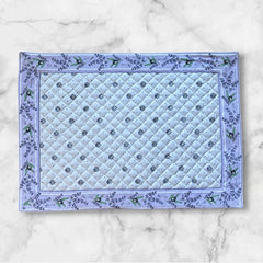 Reversible quilted cotton placemat in Lauris Light Yellow by Marat d’Avignon, featuring a white center with lavender purple floral medallions and a border of lavender sprigs and olive branches, with a white reverse side  scattered with tiny lavender  blossoms, crafted in Provence.