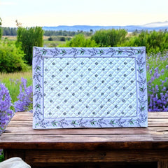 Reversible quilted cotton placemat in Lauris Light Yellow by Marat d’Avignon, featuring a white center with lavender purple floral medallions and a border of lavender sprigs and olive branches, with a white reverse side  scattered with tiny lavender  blossoms, crafted in Provence.