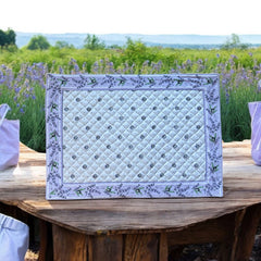 Reversible quilted cotton placemat in Lauris Light Yellow by Marat d’Avignon, featuring a white center with lavender purple floral medallions and a border of lavender sprigs and olive branches, with a white reverse side  scattered with tiny lavender  blossoms, crafted in Provence.