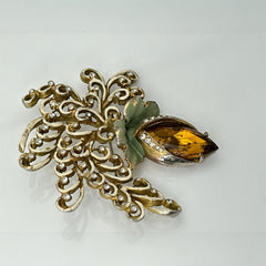 Vintage H. Pomerantz floral brooch featuring a large topaz-colored marquise rhinestone set in gold-tone metal, accented with green and cream enamel leaves and clear rhinestones; signed on the reverse, circa 1940s, measuring 3 inches by 3 inches.