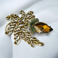 Vintage H. Pomerantz floral brooch featuring a large topaz-colored marquise rhinestone set in gold-tone metal, accented with green and cream enamel leaves and clear rhinestones; signed on the reverse, circa 1940s, measuring 3 inches by 3 inches.