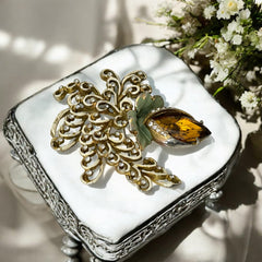 Vintage H. Pomerantz floral brooch featuring a large topaz-colored marquise rhinestone set in gold-tone metal, accented with green and cream enamel leaves and clear rhinestones; signed on the reverse, circa 1940s, measuring 3 inches by 3 inches.