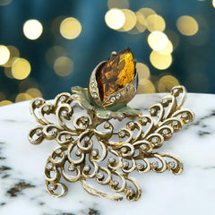 Vintage H. Pomerantz floral brooch featuring a large topaz-colored marquise rhinestone set in gold-tone metal, accented with green and cream enamel leaves and clear rhinestones; signed on the reverse, circa 1940s, measuring 3 inches by 3 inches.