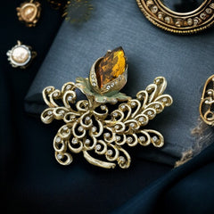 Vintage H. Pomerantz floral brooch featuring a large topaz-colored marquise rhinestone set in gold-tone metal, accented with green and cream enamel leaves and clear rhinestones; signed on the reverse, circa 1940s, measuring 3 inches by 3 inches.