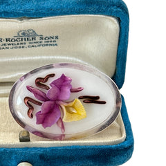 Vintage French reverse carved Lucite brooch featuring a hand-painted pink and yellow orchid on a white background. Oval shape with dimensional floral detail, excellent condition, circa 1950s.