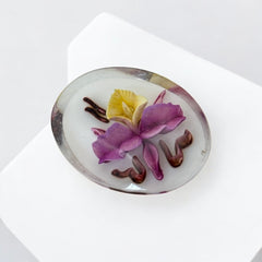 Vintage French reverse carved Lucite brooch featuring a hand-painted pink and yellow orchid on a white background. Oval shape with dimensional floral detail, excellent condition, circa 1950s.