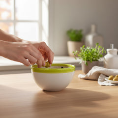 Small round ceramic bowl with green interior and rim, hand-painted with swirling olive branches, black olives, and green leaves on a beige base; measures 4 inches in diameter and 2.5 inches high.