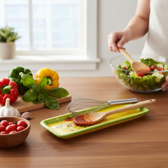 Rectangular ceramic spoon rest with yellow interior and green polka-dot rim, featuring hand-painted olive leaves, red berries, and whimsical fork and spoon motif; measures 11 by 4 inches.