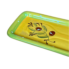 Rectangular ceramic spoon rest with yellow interior and green polka-dot rim, featuring hand-painted olive leaves, red berries, and whimsical fork and spoon motif; measures 11 by 4 inches.