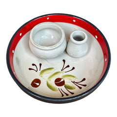 Round ceramic serving dish with red and black rim, hand-painted with green olive branches and brown olives on a cream base, accompanied by two small matching vessels nested inside.