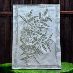 Provence tea towel featuring an olive branch with fruits and flowers at the center, framed by the repeated text 'L'Écomusée de l'Olivier.' Woven in olive green on a natural background with a 100% cotton composition, blending rustic charm and elegance.