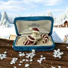 Vintage gold-tone brooch featuring Santa Claus in red and white enamel, riding a striped candy cane with green accent; 1980s/90s holiday design, photographed on neutral background.
