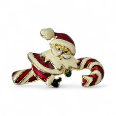 Vintage gold-tone brooch featuring Santa Claus in red and white enamel, riding a striped candy cane with green accent; 1980s/90s holiday design, photographed on neutral background.