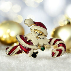 Vintage gold-tone brooch featuring Santa Claus in red and white enamel, riding a striped candy cane with green accent; 1980s/90s holiday design, photographed on neutral background.