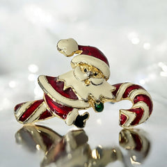 Vintage gold-tone brooch featuring Santa Claus in red and white enamel, riding a striped candy cane with green accent; 1980s/90s holiday design, photographed on neutral background.