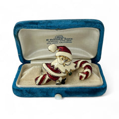 Vintage gold-tone brooch featuring Santa Claus in red and white enamel, riding a striped candy cane with green accent; 1980s/90s holiday design, photographed on neutral background.
