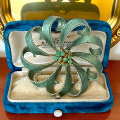 Vintage 1960s floral brooch with light green enamel ribbon petals, gold tone rope edges, and rhinestone center.