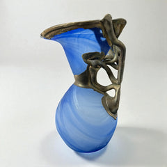 Signed Romanian handblown art glass vase from the 1990s featuring swirling blue glass and sculptural bronze overlay with organic vine-like forms. The vase has a flared top, narrow base, and an undeciphered artist’s signature etched into the glass. A collectible decorative piece in very good vintage condition.