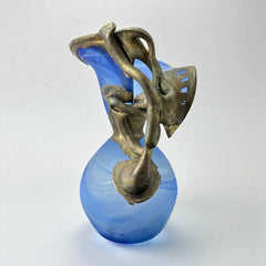 Signed Romanian handblown art glass vase from the 1990s featuring swirling blue glass and sculptural bronze overlay with organic vine-like forms. The vase has a flared top, narrow base, and an undeciphered artist’s signature etched into the glass. A collectible decorative piece in very good vintage condition.