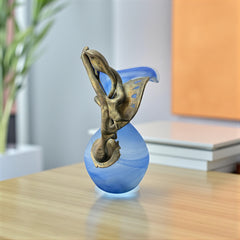 Signed Romanian handblown art glass vase from the 1990s featuring swirling blue glass and sculptural bronze overlay with organic vine-like forms. The vase has a flared top, narrow base, and an undeciphered artist’s signature etched into the glass. A collectible decorative piece in very good vintage condition.