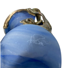 Signed Romanian handblown art glass vase from the 1990s featuring swirling blue glass and sculptural bronze overlay with organic vine-like forms. The vase has a flared top, narrow base, and an undeciphered artist’s signature etched into the glass. A collectible decorative piece in very good vintage condition.