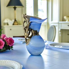 Signed Romanian handblown art glass vase from the 1990s featuring swirling blue glass and sculptural bronze overlay with organic vine-like forms. The vase has a flared top, narrow base, and an undeciphered artist’s signature etched into the glass. A collectible decorative piece in very good vintage condition.