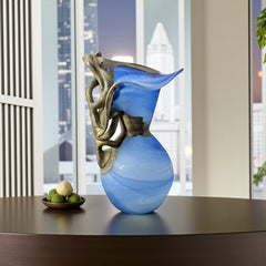 Signed Romanian handblown art glass vase from the 1990s featuring swirling blue glass and sculptural bronze overlay with organic vine-like forms. The vase has a flared top, narrow base, and an undeciphered artist’s signature etched into the glass. A collectible decorative piece in very good vintage condition.