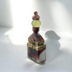Vintage Romanian art glass perfume bottle with a plum and yellow frosted body, square base, and rounded neck, adorned with bronze wire and a sculptural stopper featuring a translucent yellow-green bead and plum-toned top.