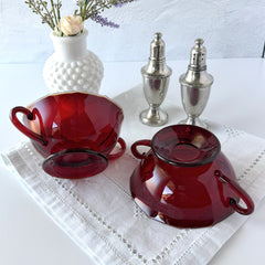 Vintage ruby red double‑handled footed glass bowls with paneled design and subtle amber rim, shown in natural light for color and detail.