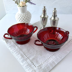 Vintage ruby red double‑handled footed glass bowls with paneled design and subtle amber rim, shown in natural light for color and detail.