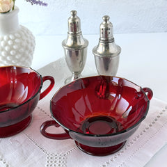 Vintage ruby red double‑handled footed glass bowls with paneled design and subtle amber rim, shown in natural light for color and detail.
