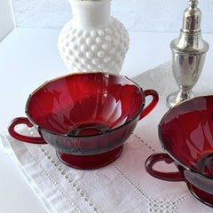Vintage ruby red double‑handled footed glass bowls with paneled design and subtle amber rim, shown in natural light for color and detail.