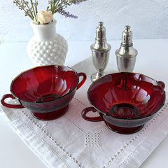 Vintage ruby red double‑handled footed glass bowls with paneled design and subtle amber rim, shown in natural light for color and detail.