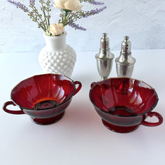 Vintage ruby red double‑handled footed glass bowls with paneled design and subtle amber rim, shown in natural light for color and detail.