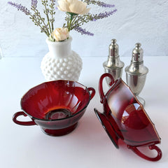 Vintage ruby red double‑handled footed glass bowls with paneled design and subtle amber rim, shown in natural light for color and detail.