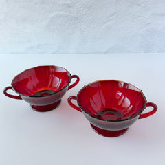 Vintage ruby red double‑handled footed glass bowls with paneled design and subtle amber rim, shown in natural light for color and detail.