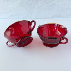 Vintage ruby red double‑handled footed glass bowls with paneled design and subtle amber rim, shown in natural light for color and detail.