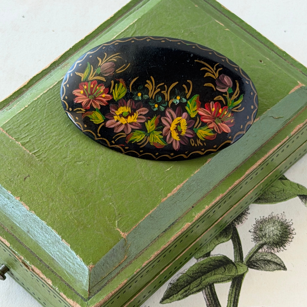 Vintage Russian hand‑painted floral black lacquer oval brooch with red, pink, and yellow flowers and gold detailing.
