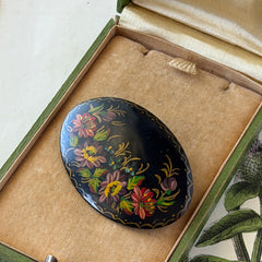 Vintage Russian hand‑painted floral black lacquer oval brooch with red, pink, and yellow flowers and gold detailing.