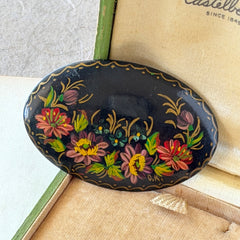 Vintage Russian hand‑painted floral black lacquer oval brooch with red, pink, and yellow flowers and gold detailing.