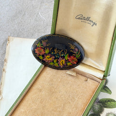 Vintage Russian hand‑painted floral black lacquer oval brooch with red, pink, and yellow flowers and gold detailing.