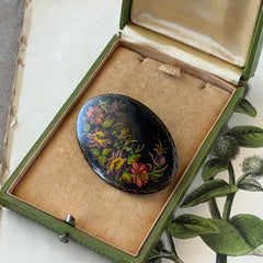 Vintage Russian hand‑painted floral black lacquer oval brooch with red, pink, and yellow flowers and gold detailing.